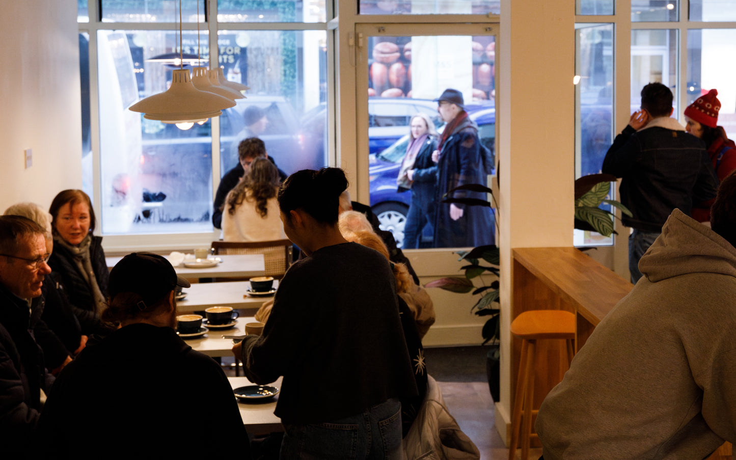 A busy caffe, barista serving a coffee to atable. Mid day light come, fogged up windows.