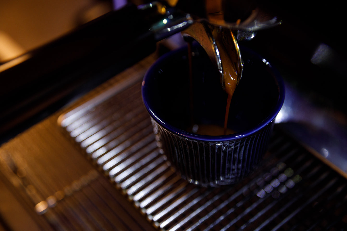 Espresso shot extraction, into a deep blue reflective cup with consecutive straight ridges.