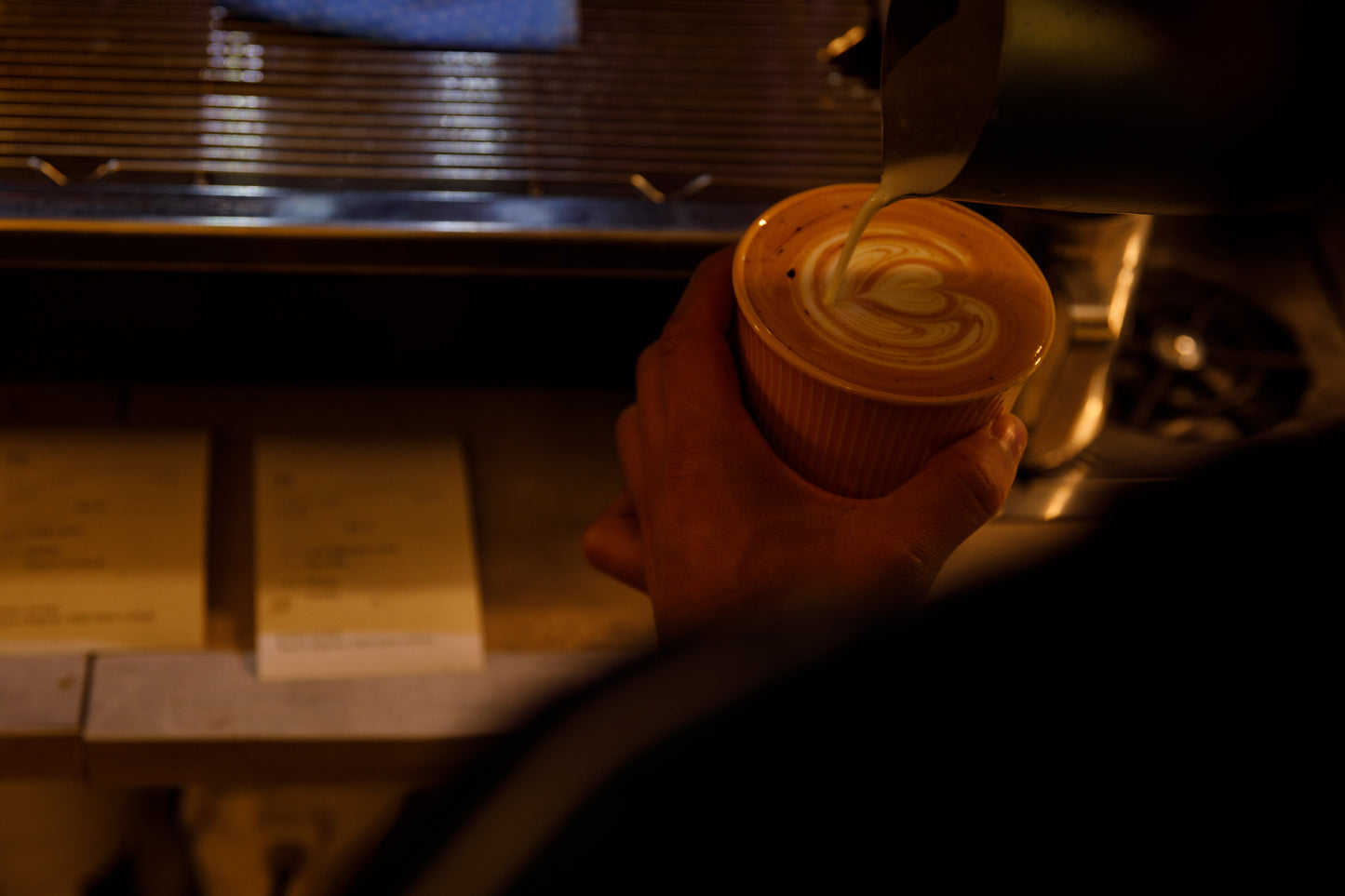 Barista making latte art. Tulip variation. Order checks to the left and coffee machine infront.