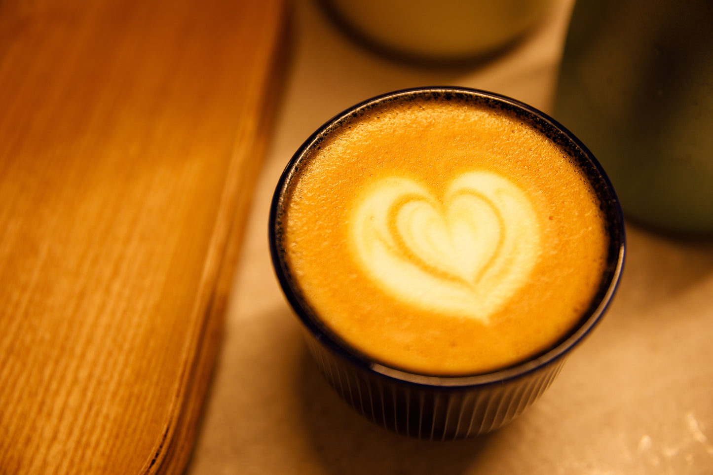 Love-shaped design on a latte, a wooden board to the left and a milk jar.
