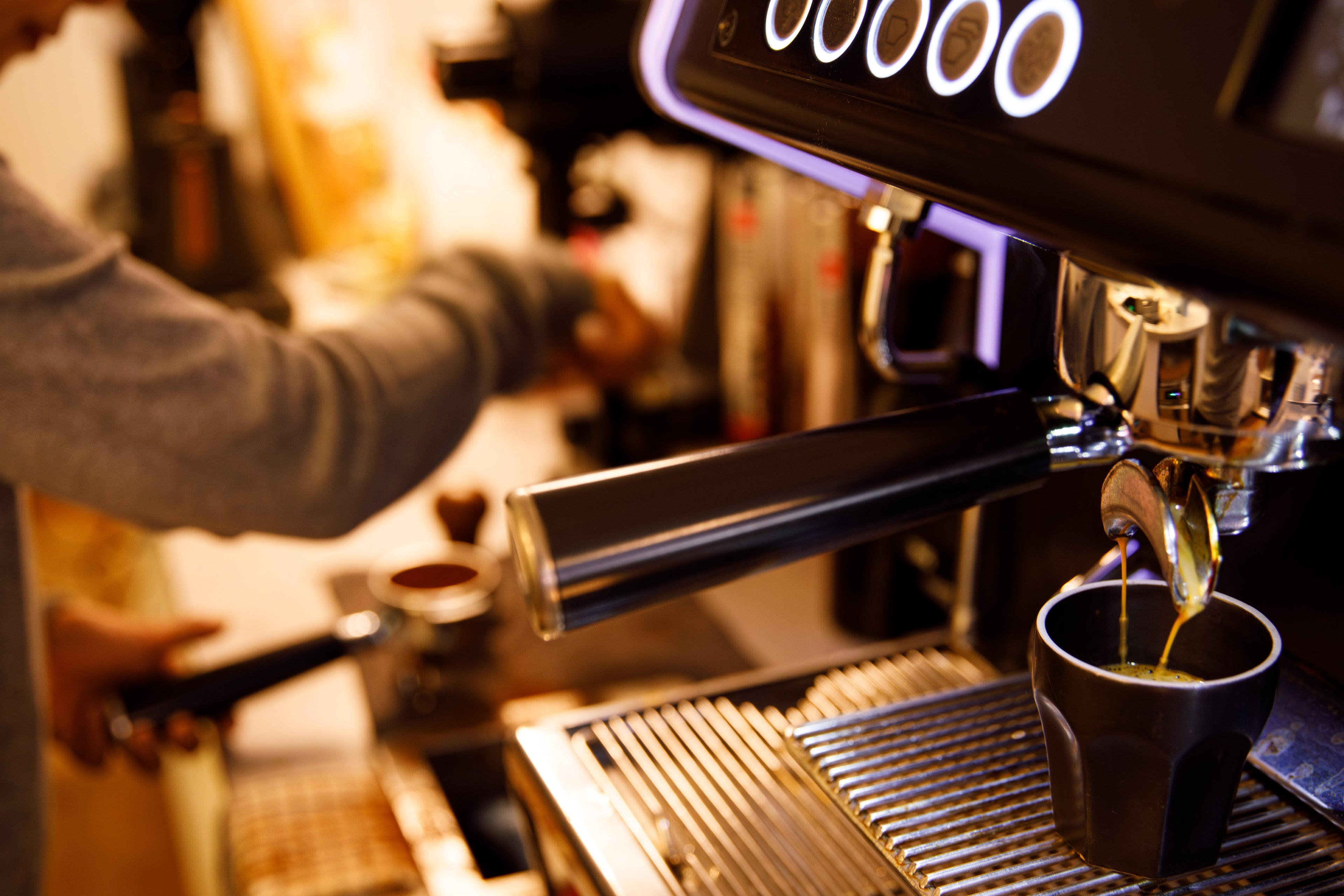 Coffee machine, double shot pull. Barista tamping ground beans in background.