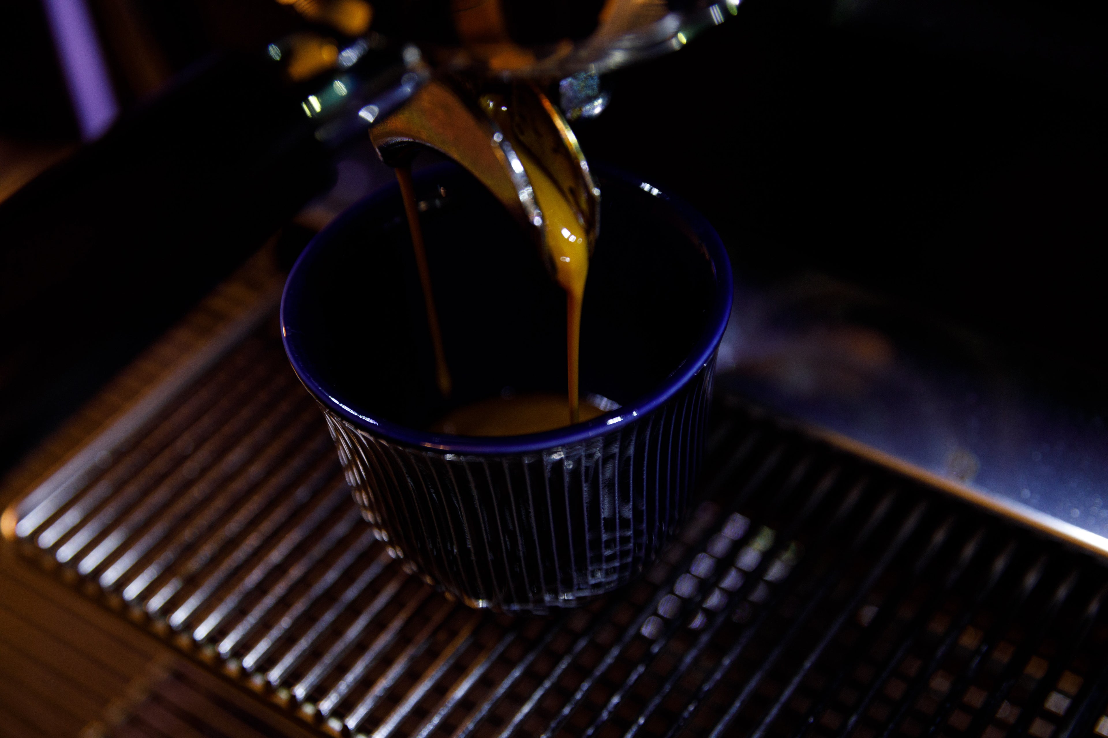Espresso shot extraction, into a deep blue reflective cup with consecutive straight ridges.